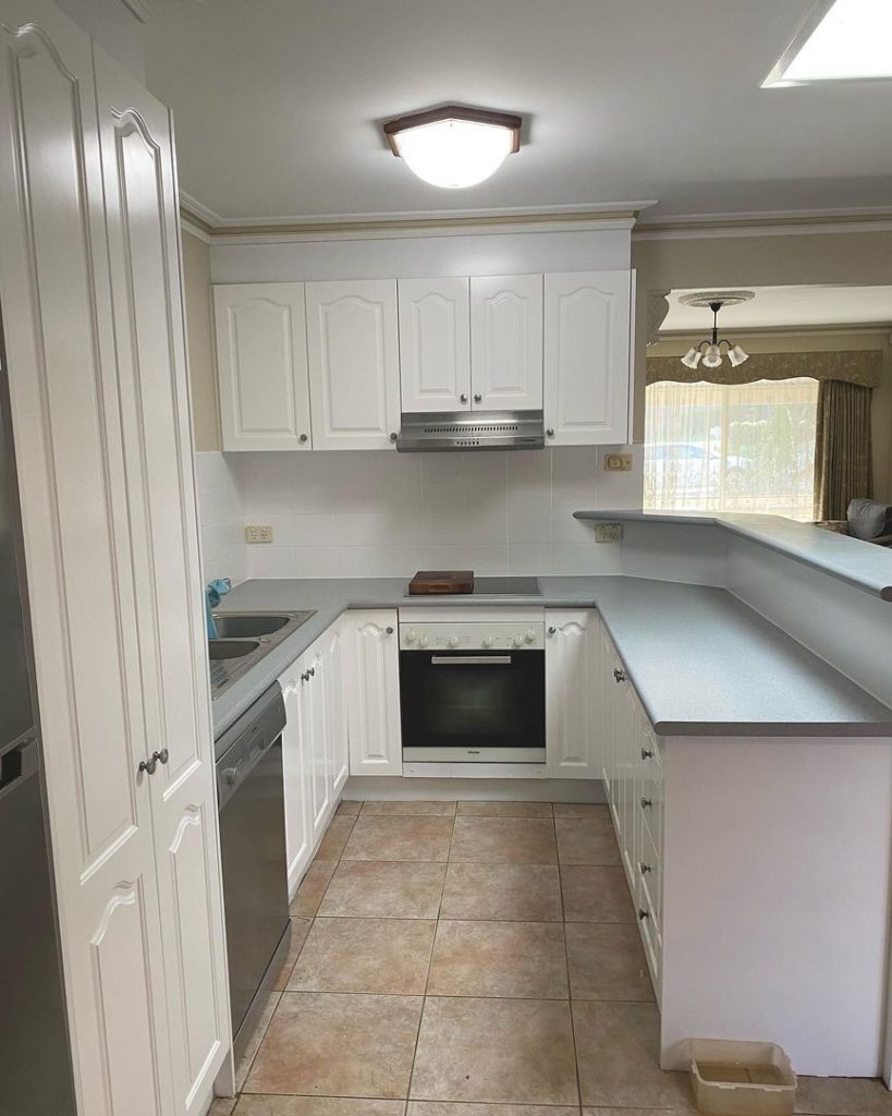 Modern kitchen with white cabinets, stainless steel appliances, grey countertops, and beige tile flooring.