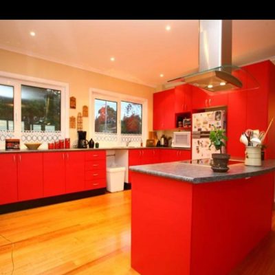 Modern kitchen with red cabinets, grey countertops, wooden flooring, and stainless steel appliances.