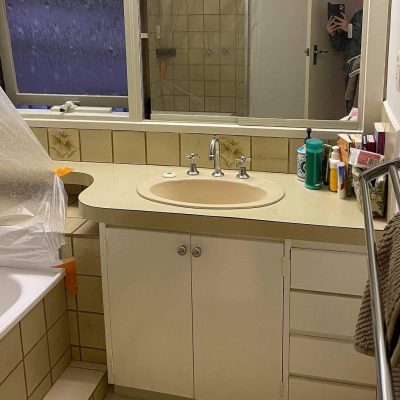 Bathroom with beige sink, plastic-covered bathtub, floral tiles, and toiletries on counter.