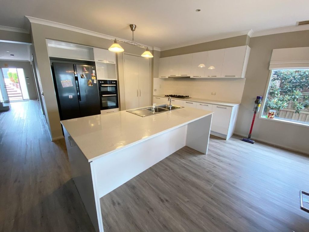 Renovated kitchen with central island, black appliances, white cabinets, and light wood flooring.