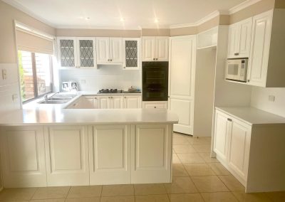 Renovated kitchen with white cabinets, black double oven, gas stovetop, stainless steel sink under a window, and large kitchen island.