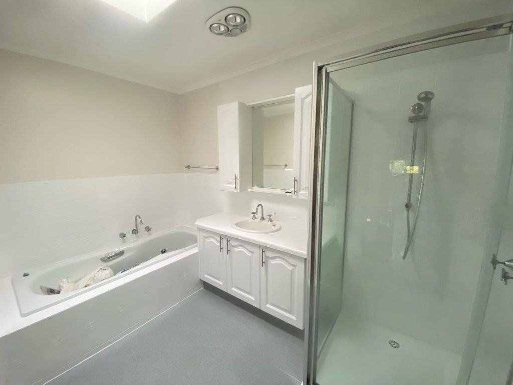 Renovated bathroom with bathtub, glass-enclosed shower, and vanity unit.