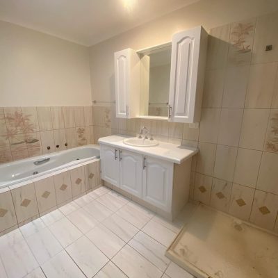 Renovated bathroom with white bathtub, vanity unit, and beige decorative tiles.