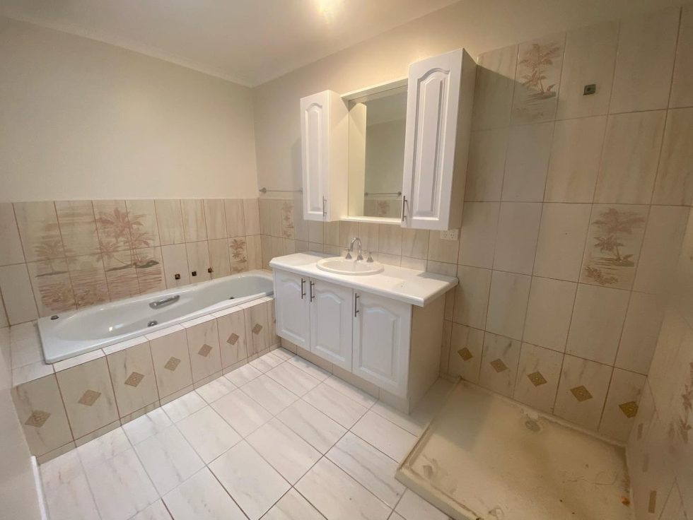 Renovated bathroom with white bathtub, vanity unit, and beige decorative tiles.