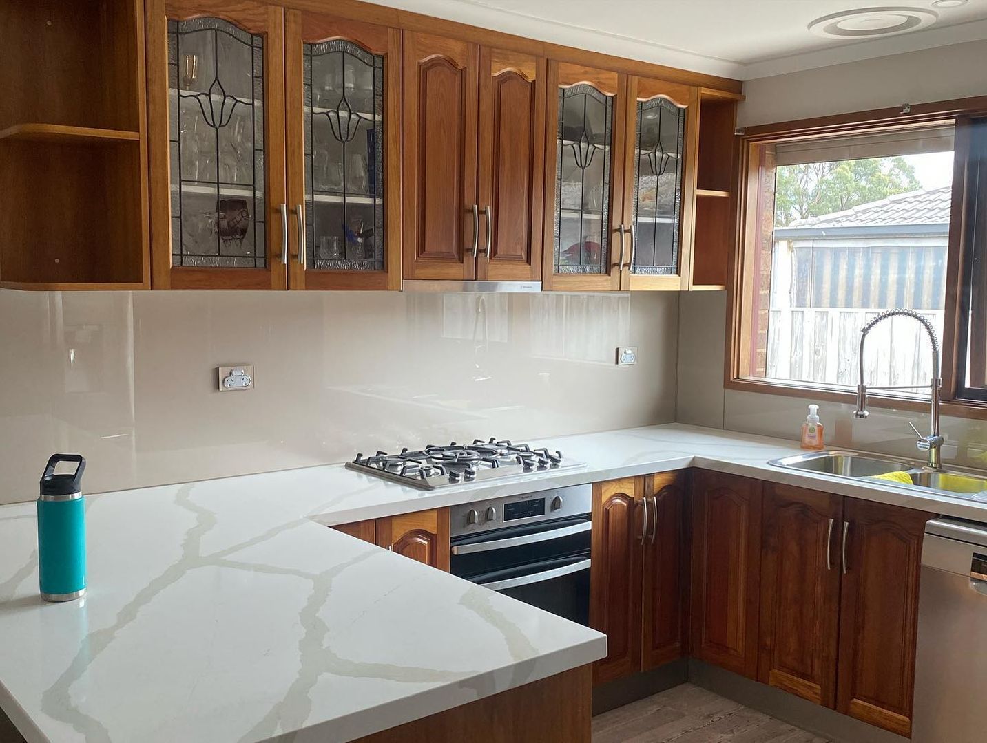 Renovated kitchen with wooden cabinets, marble countertops, stainless steel appliances, and a large window.