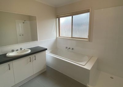 Bathroom with sink, countertop, bathtub under a window, and a shower area.