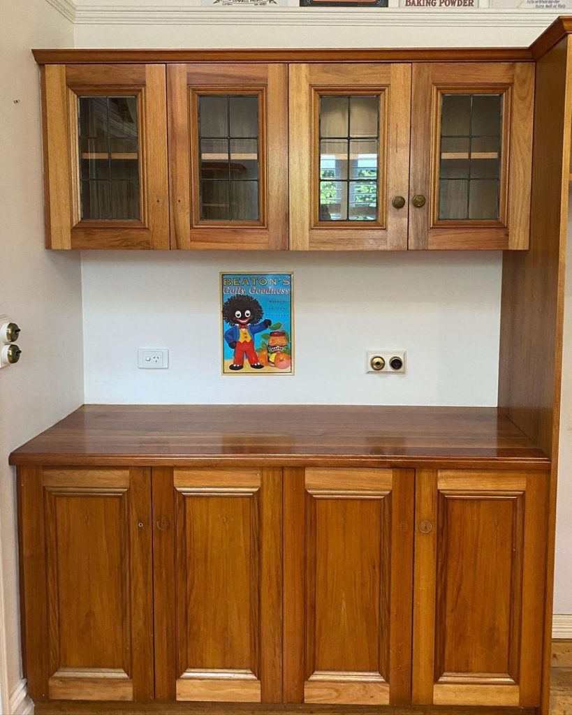 Wooden kitchen cabinets with glass-paneled doors, a polished countertop, and a vintage poster on the wall.