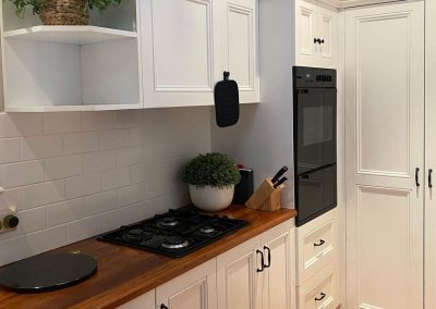 Remodeled kitchen featuring white cabinets, wooden countertops, gas stovetop, built-in oven, and decorative plants.