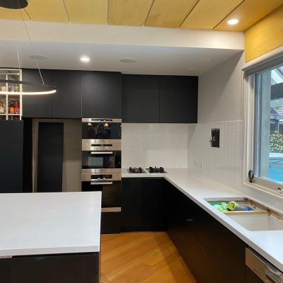 Modern kitchen with black cabinets, white countertops, built-in appliances, and wooden flooring.