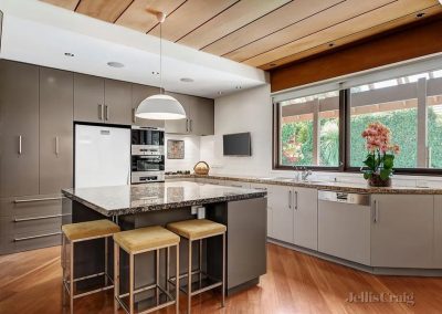Modern kitchen with granite island, built-in appliances, grey cabinets, wooden floor, and large window.
