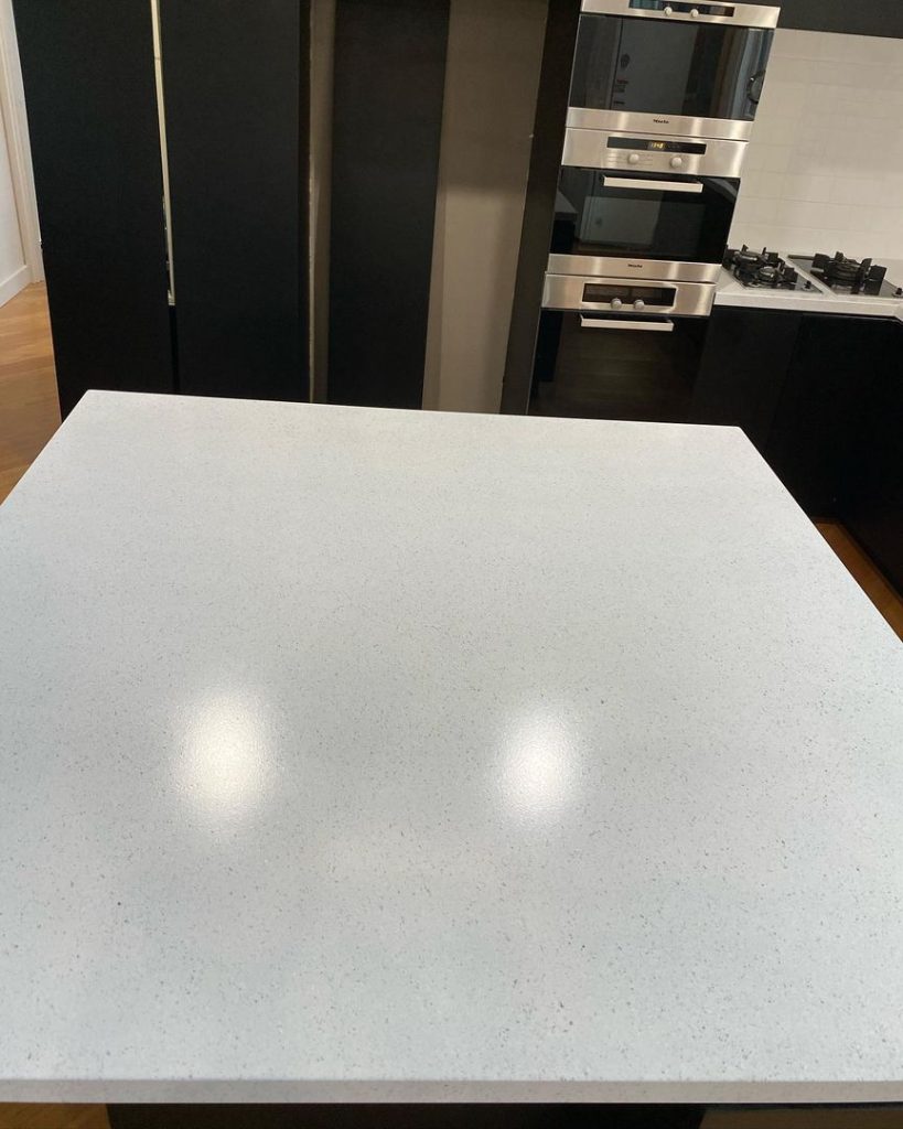 White speckled countertop in a modern kitchen with black cabinets and stainless steel appliances.