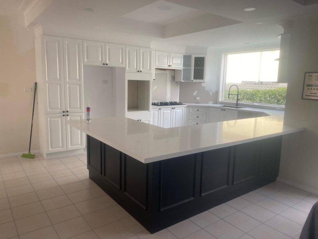 Modern kitchen with large island, white cabinets, built-in stovetop, and large window providing natural light.