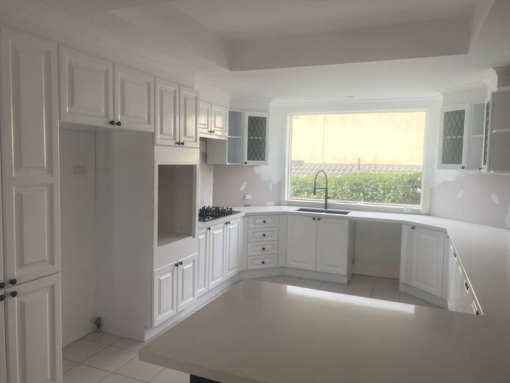 White kitchen with new cabinets, large window, and central island under renovation.