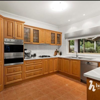 Modern kitchen with wooden cabinetry, stainless steel appliances, white subway tile backsplash, and terracotta flooring.